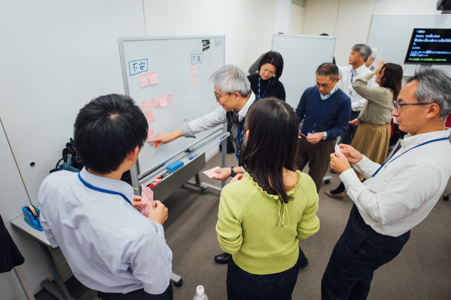 研修で、デフ社員と聴者の参加者がホワイトボードを囲み、「不安」「不満」と書かれた欄に付箋を貼りながら意見交換している様子。