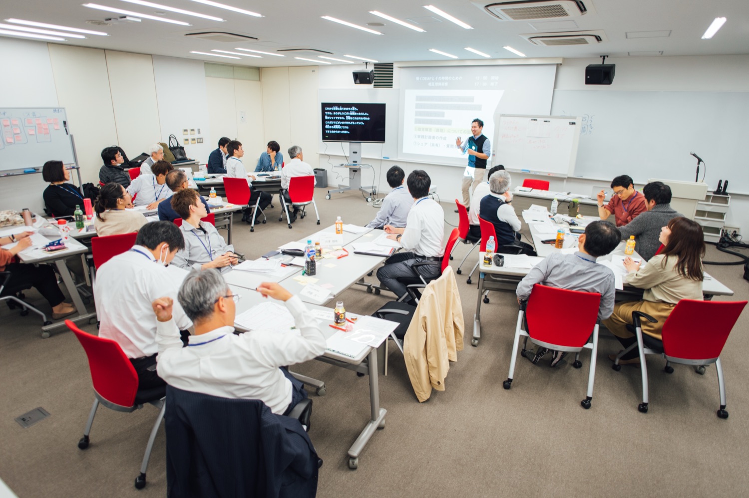 デフビズの研修風景。コの字に並んだ机を囲み、約20名の企業の参加者が前方のスクリーンを見ながら受講している様子。